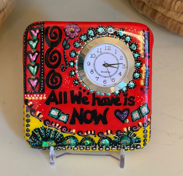 Decorative clock with colorful design and text "All We Have Is Now" on a stand