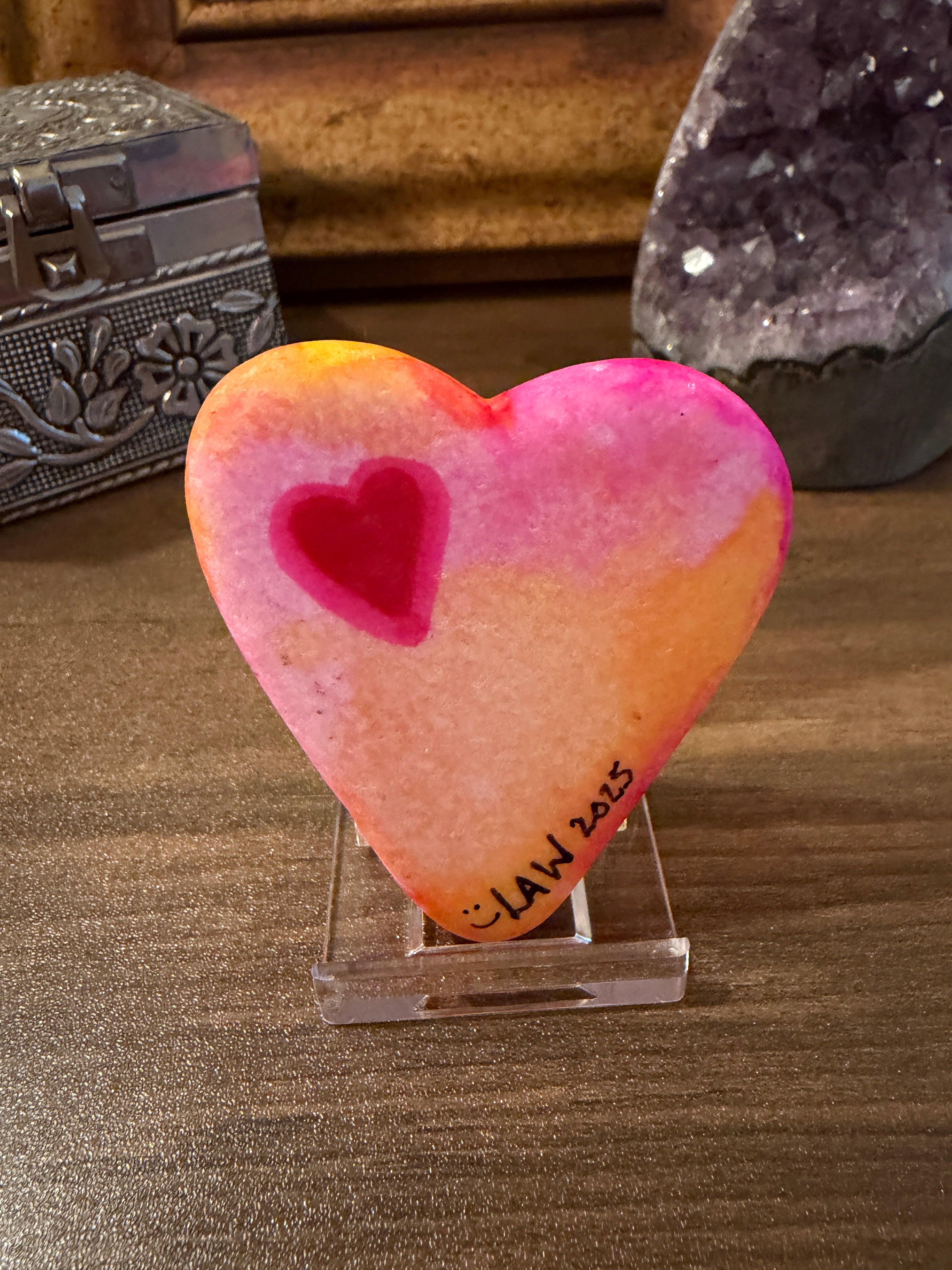 Heart-shaped painted stone with a pink and orange gradient on a textured surface
