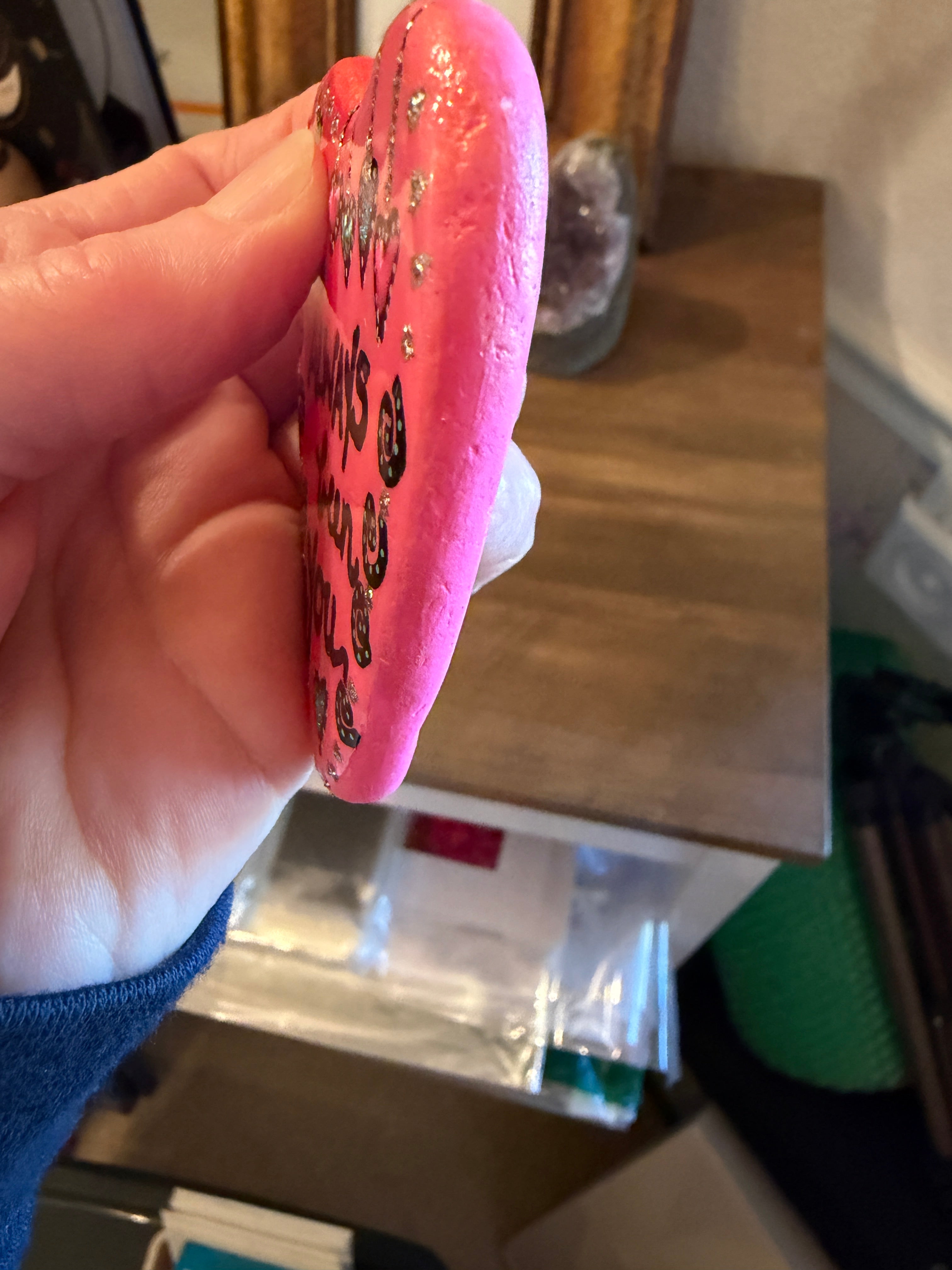 Pink painted heart stone held in a hand against a blurred indoor background