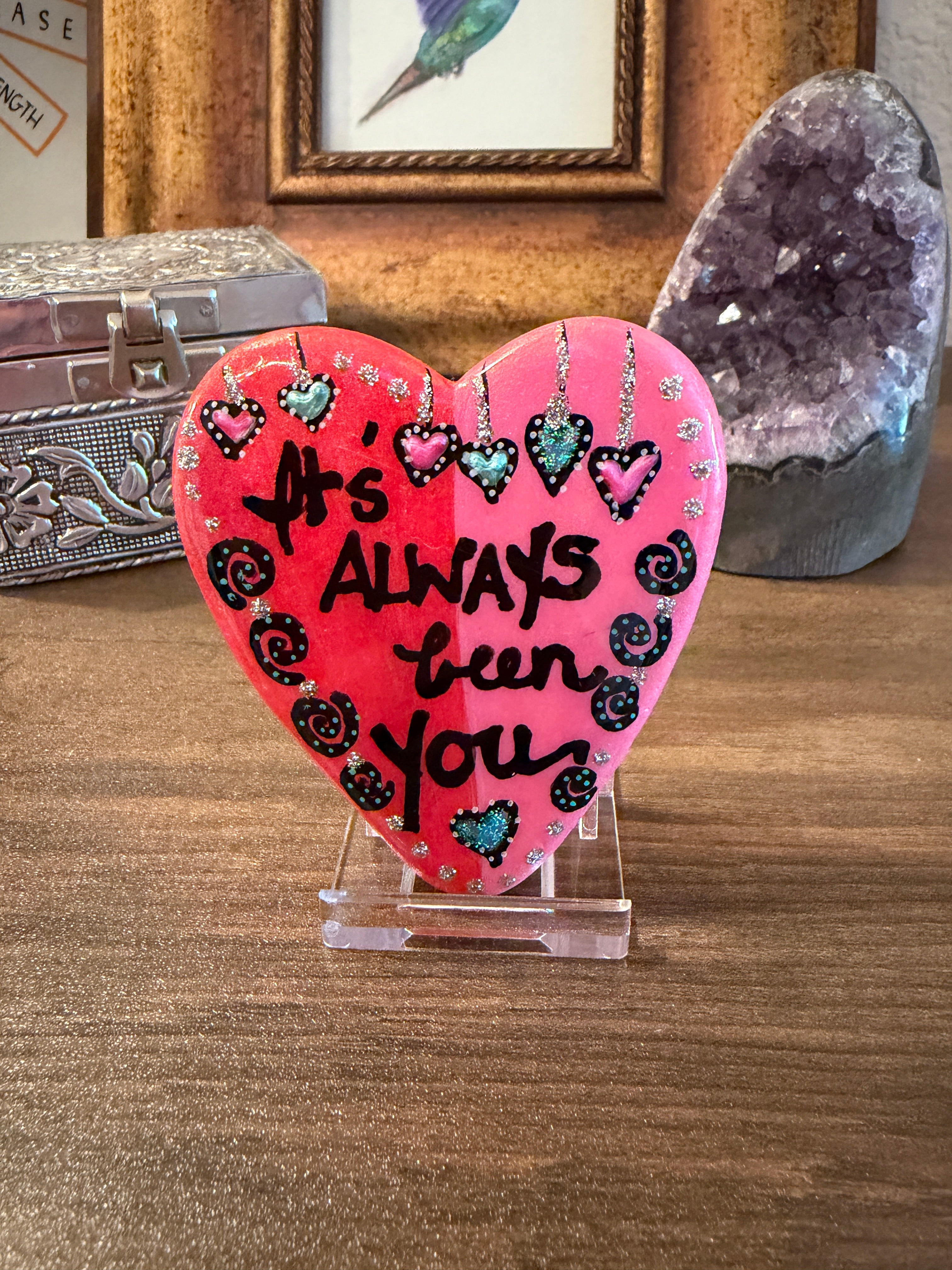Heart-shaped painted stone with 'It's Always Been You' text on a wooden surface