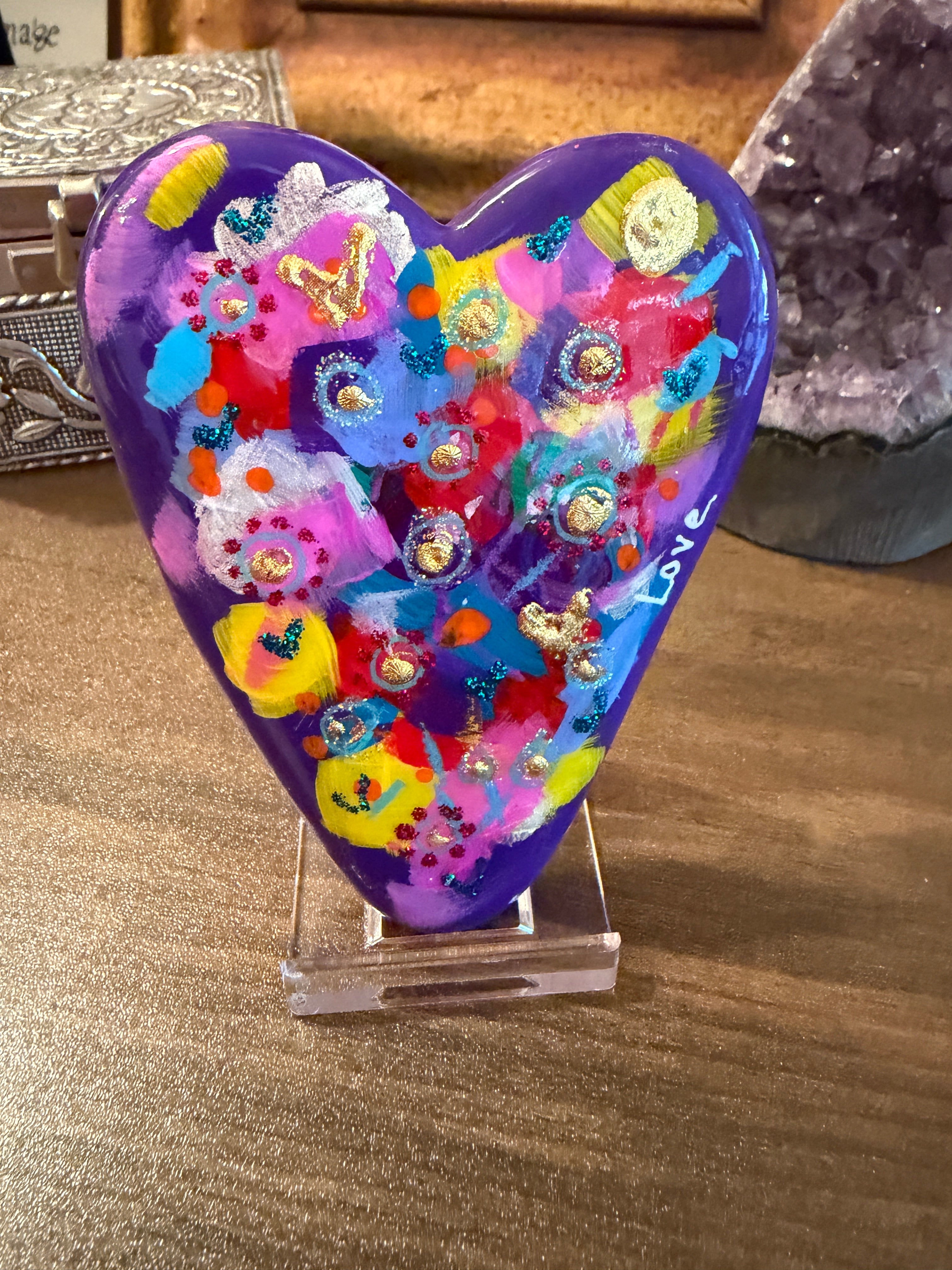 Colorful heart-shaped painted stone with floral patterns on a wooden surface