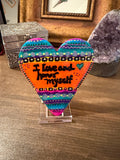 Colorful heart-shaped painted stone with text on a wooden surface
