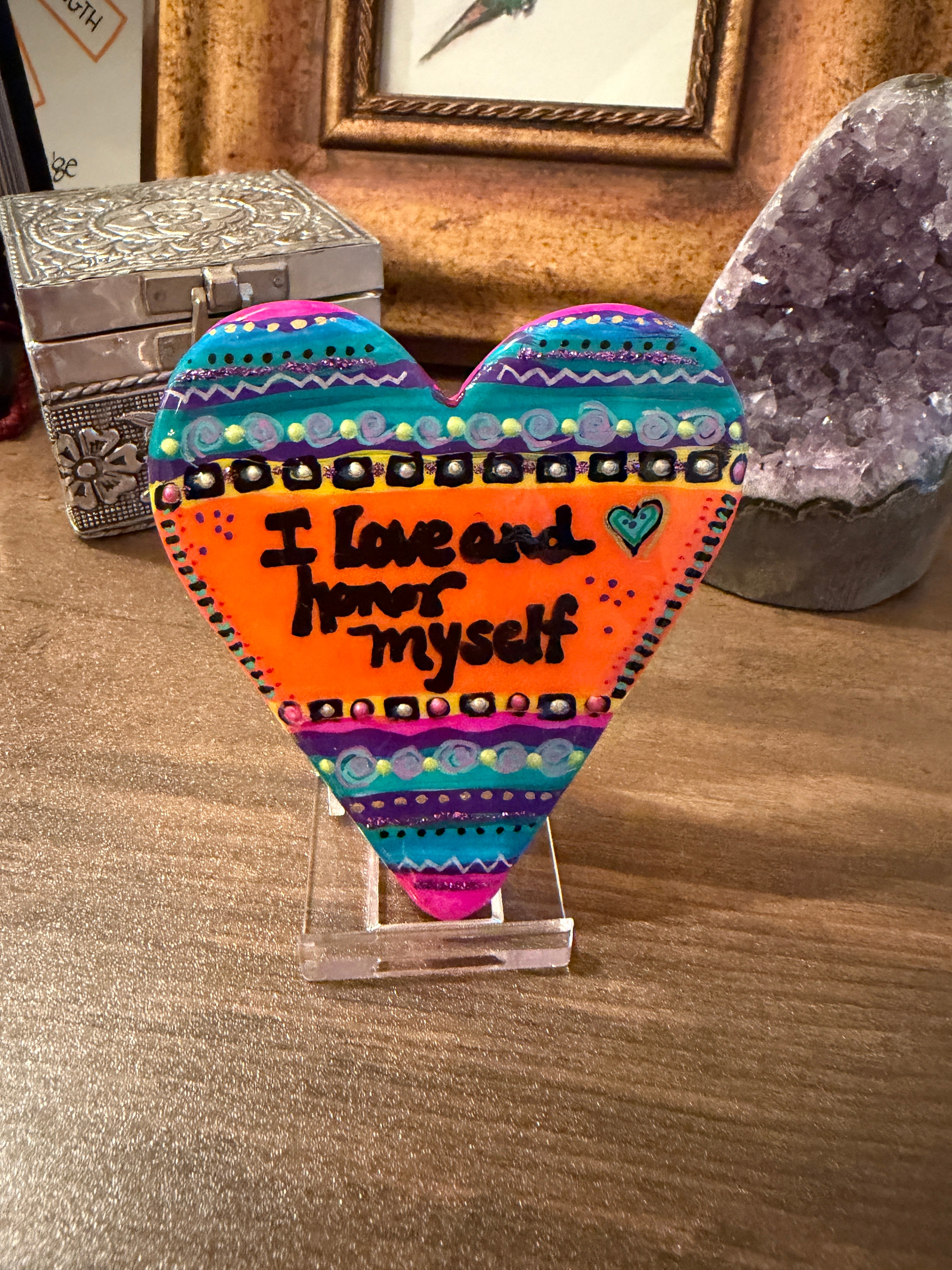 Colorful heart-shaped painted stone with text on a wooden surface