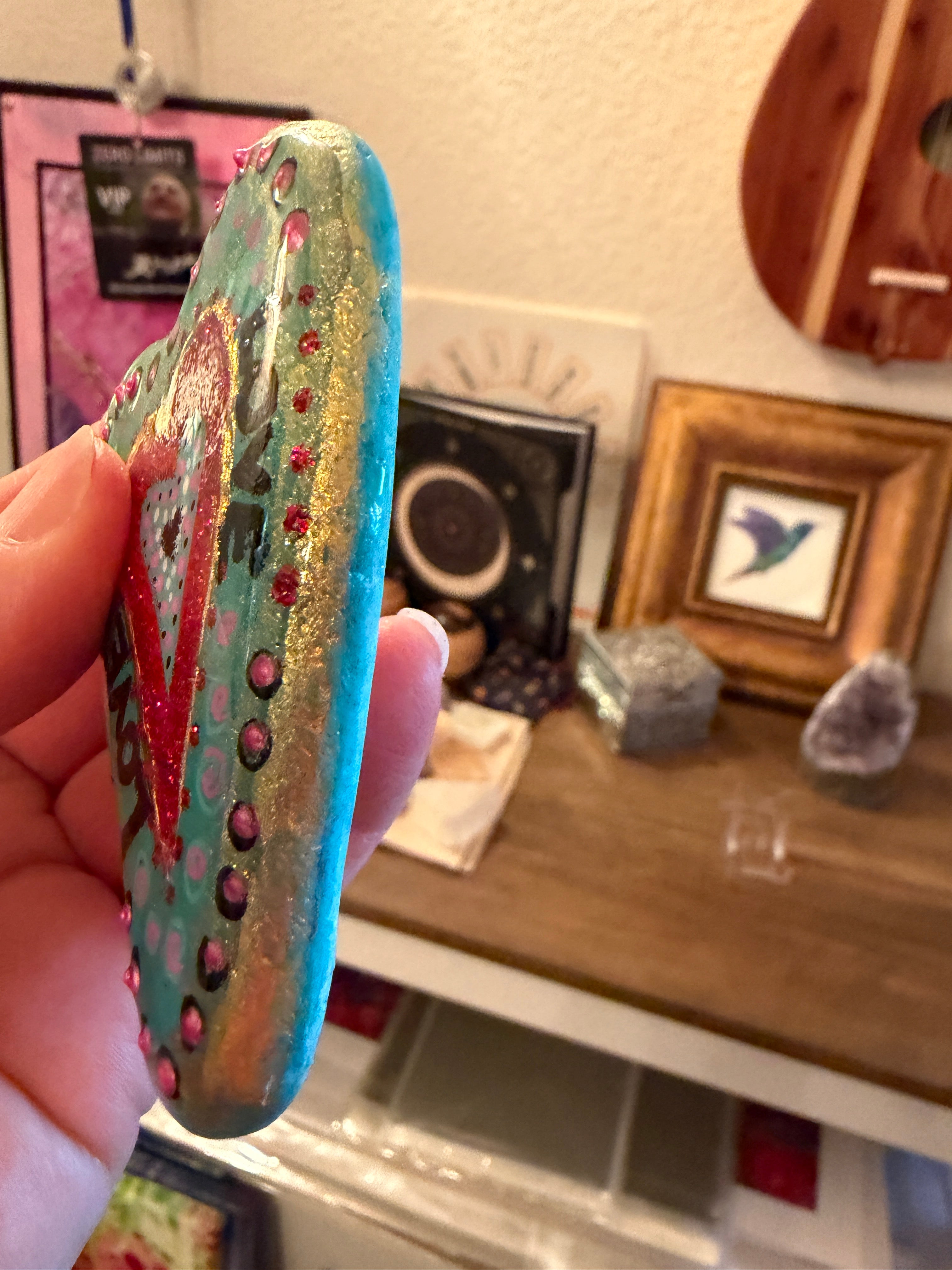 Colorful painted heart held by a hand with a blurred indoor background
