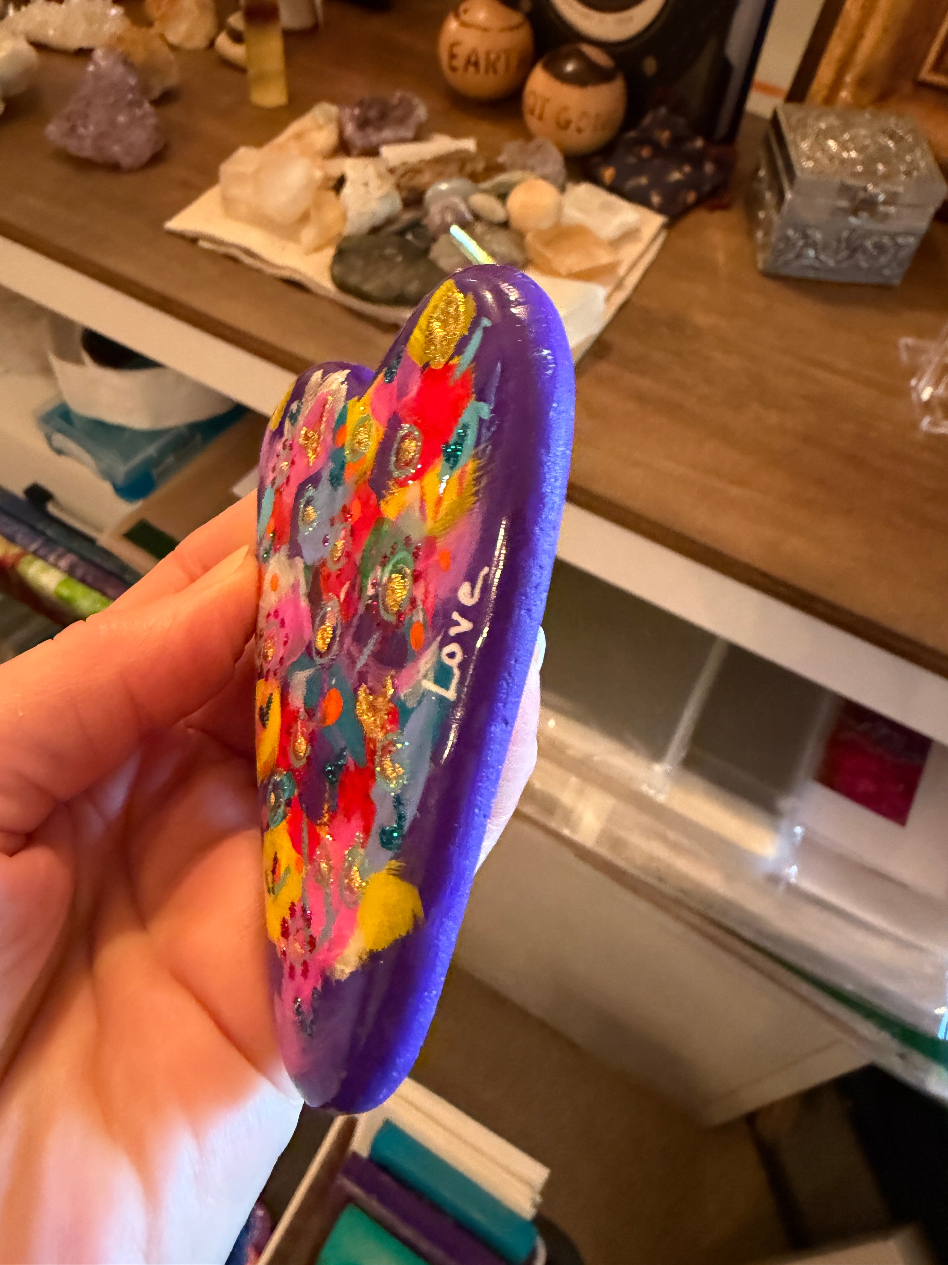 Colorful painted heart with bold design held in a hand, blurred background