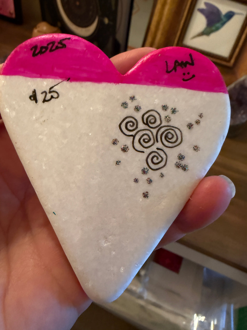 Painted heart stone with pink and black patterns held by a hand