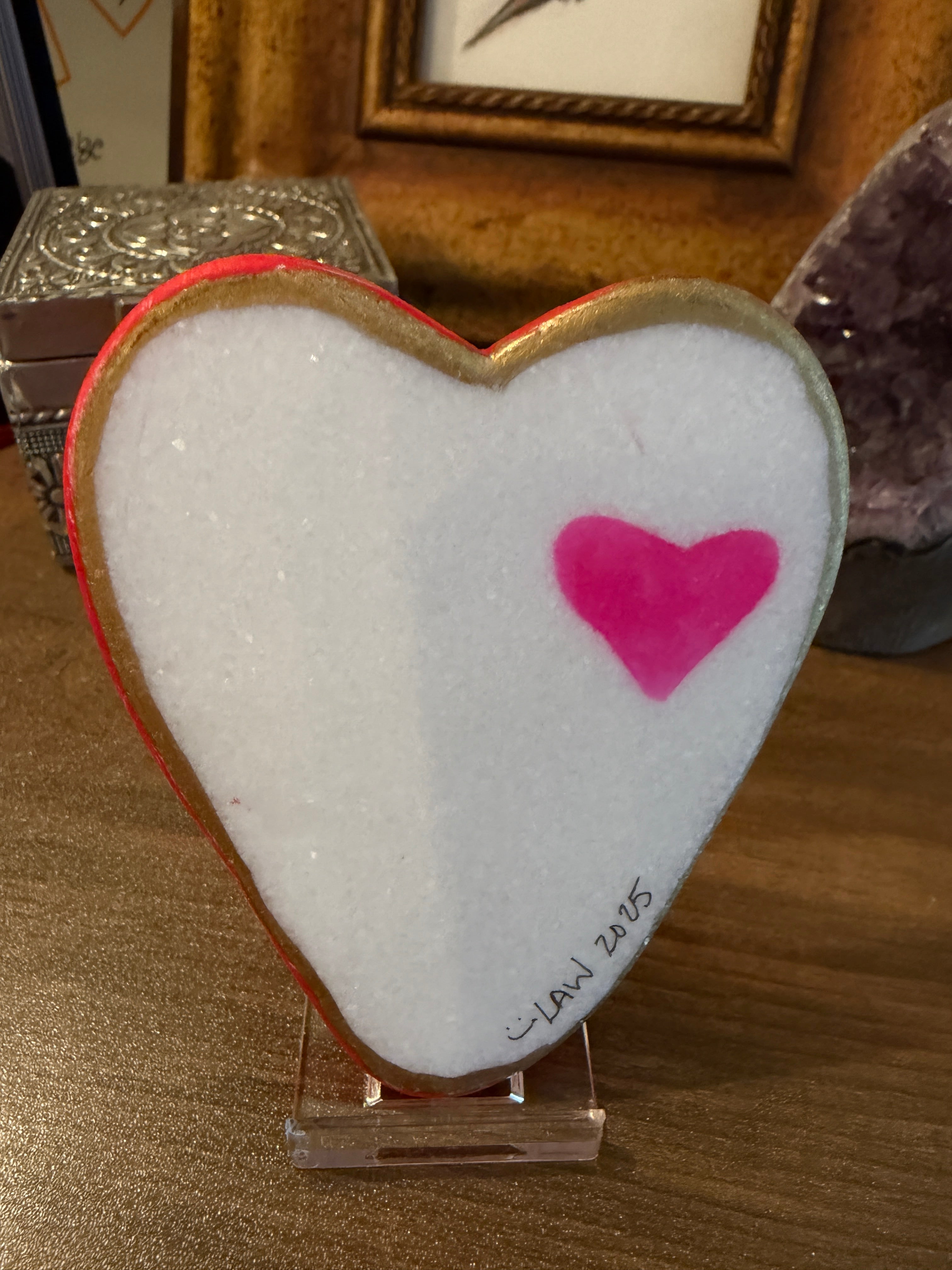 Heart-shaped painted stone with a pink heart on a wooden surface