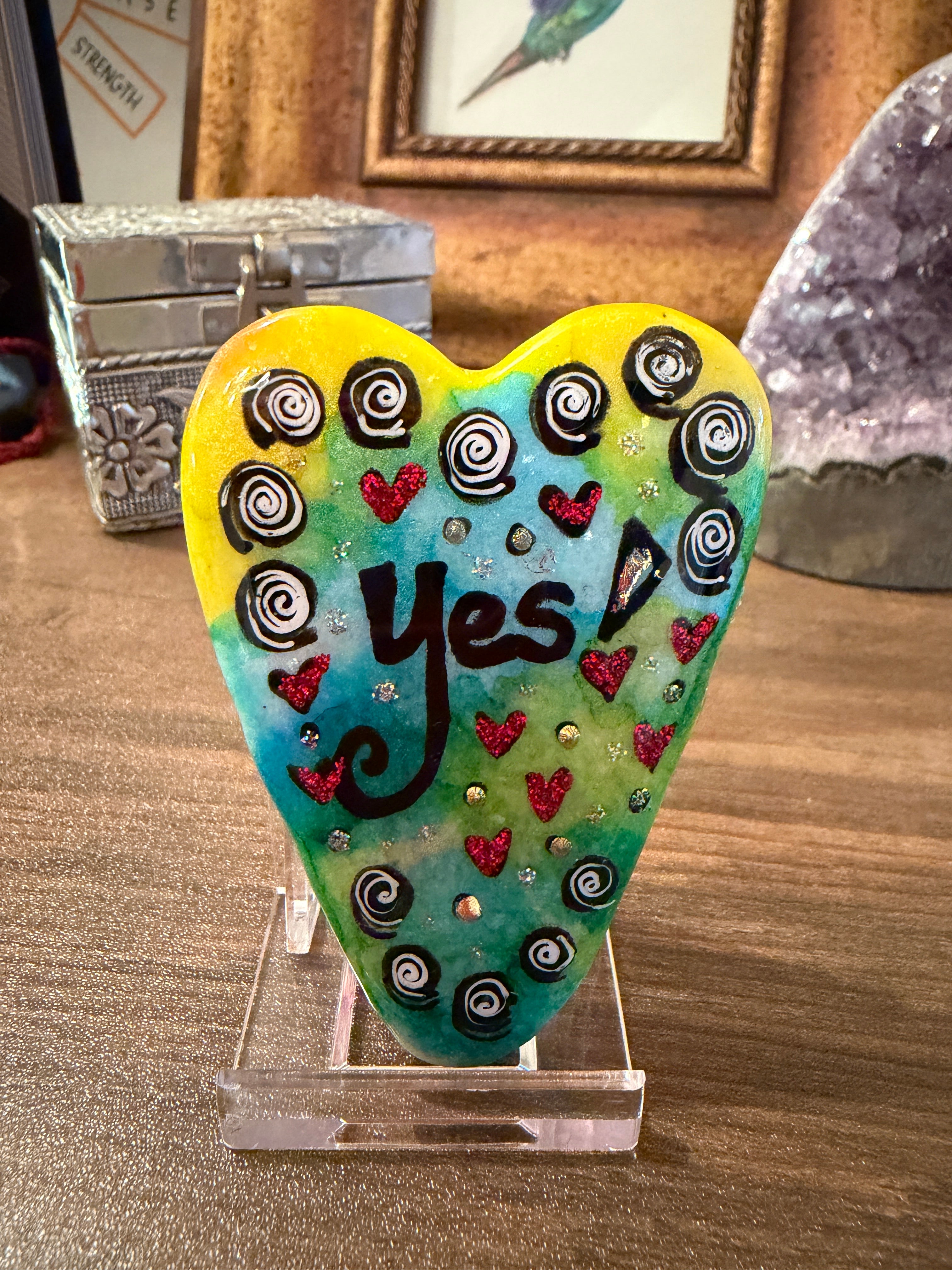 Colorful heart-shaped painted stone with 'Yes' text on a wooden surface