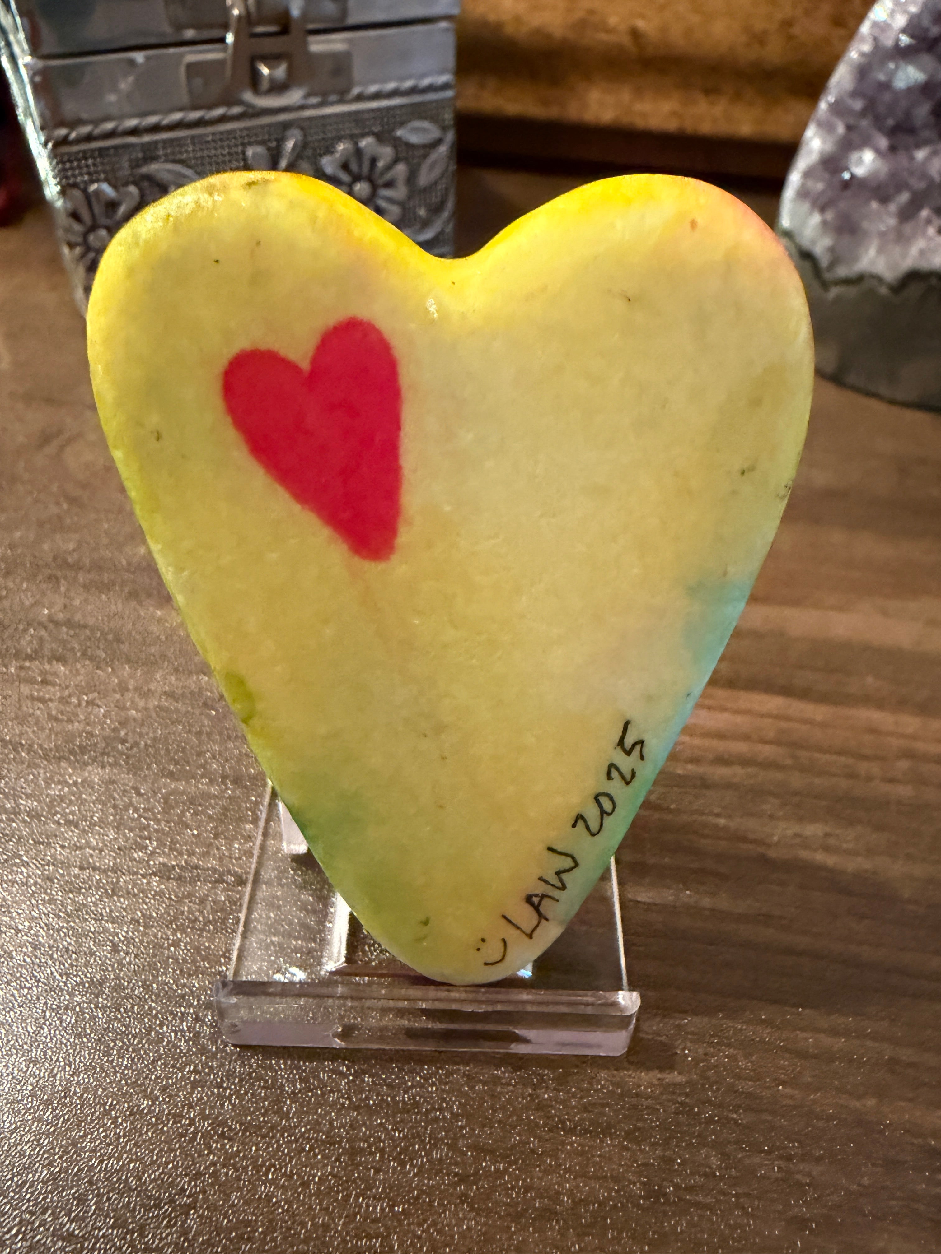 Heart-shaped yellow painted stone with a red heart on a wooden surface