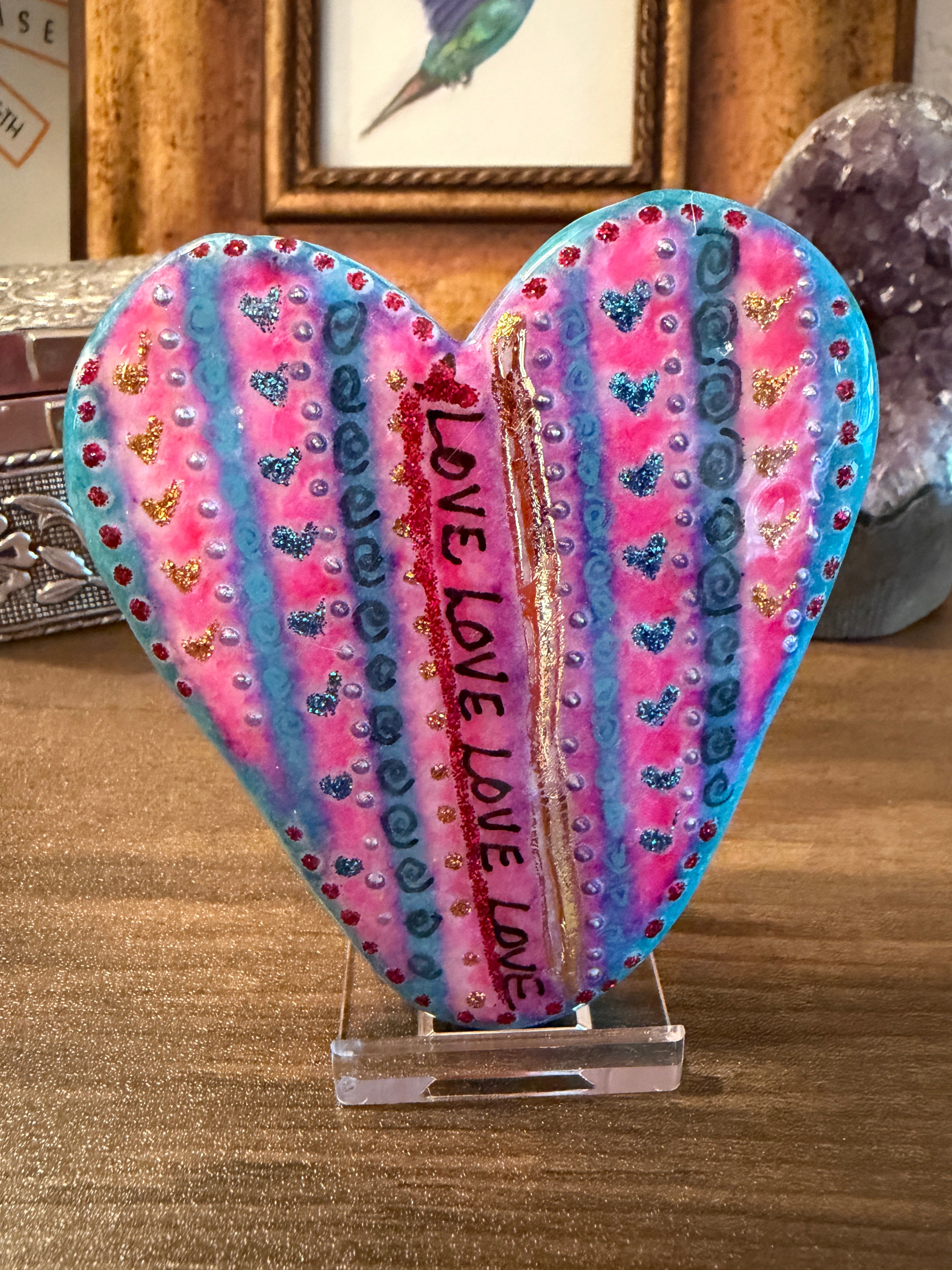 Heart-shaped painted stone with 'LOVE' text and colorful patterns on a wooden surface.
