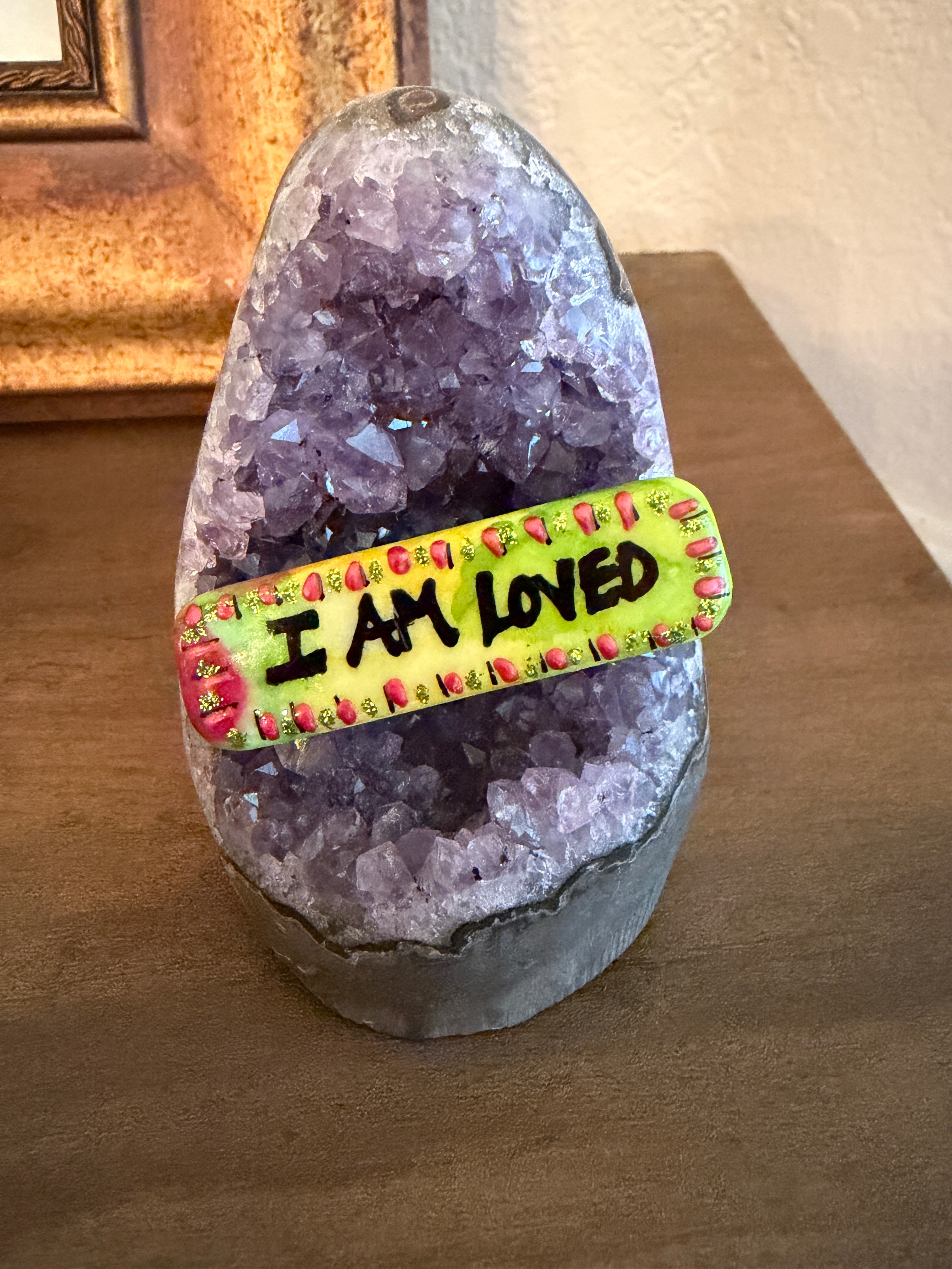 Hand-painted stone with the affirmation 'I am loved' resting on an amethyst base