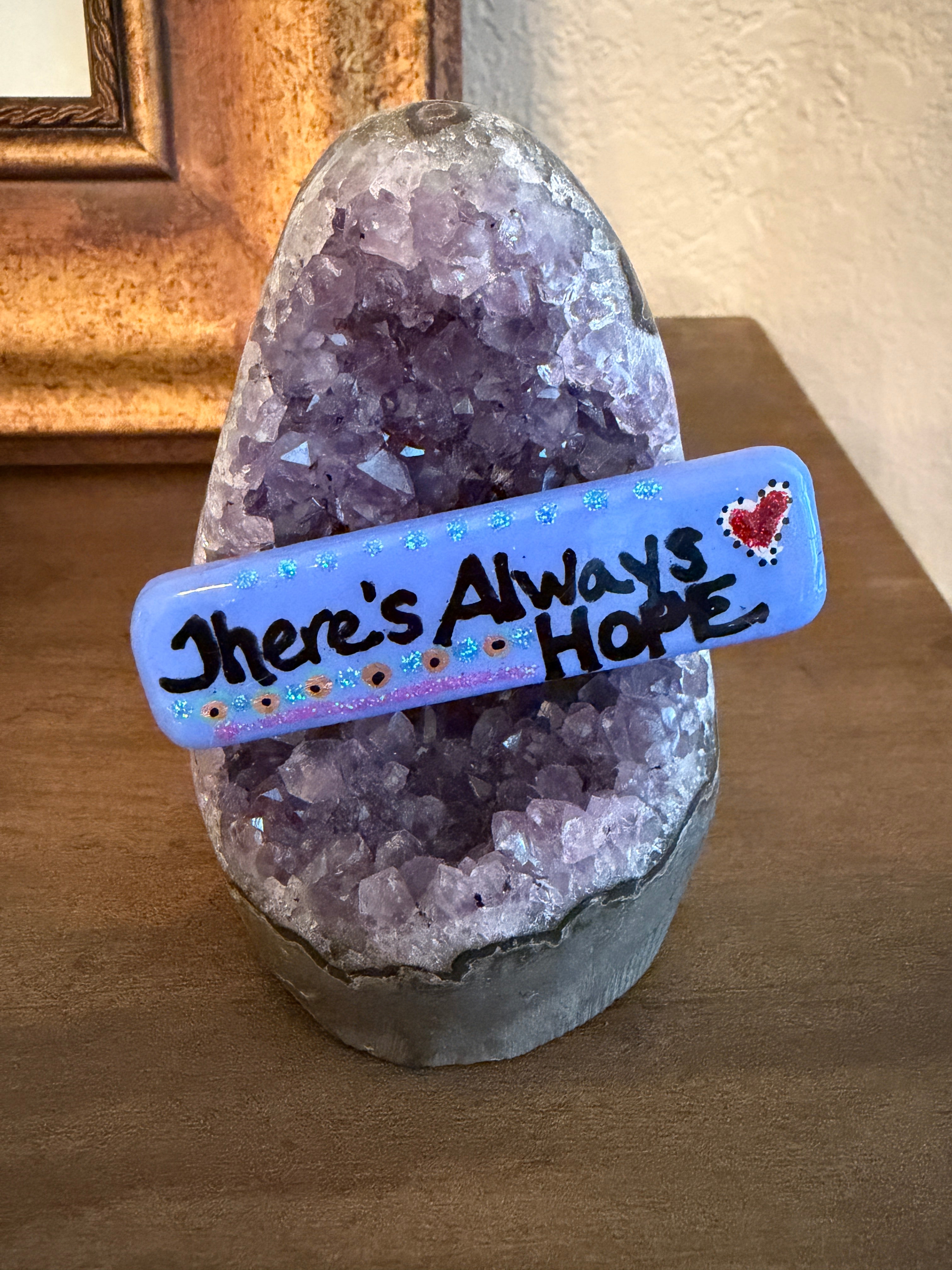 Small, hand-painted stone with the intention "There's Always Hope' text on an amethyst stand.