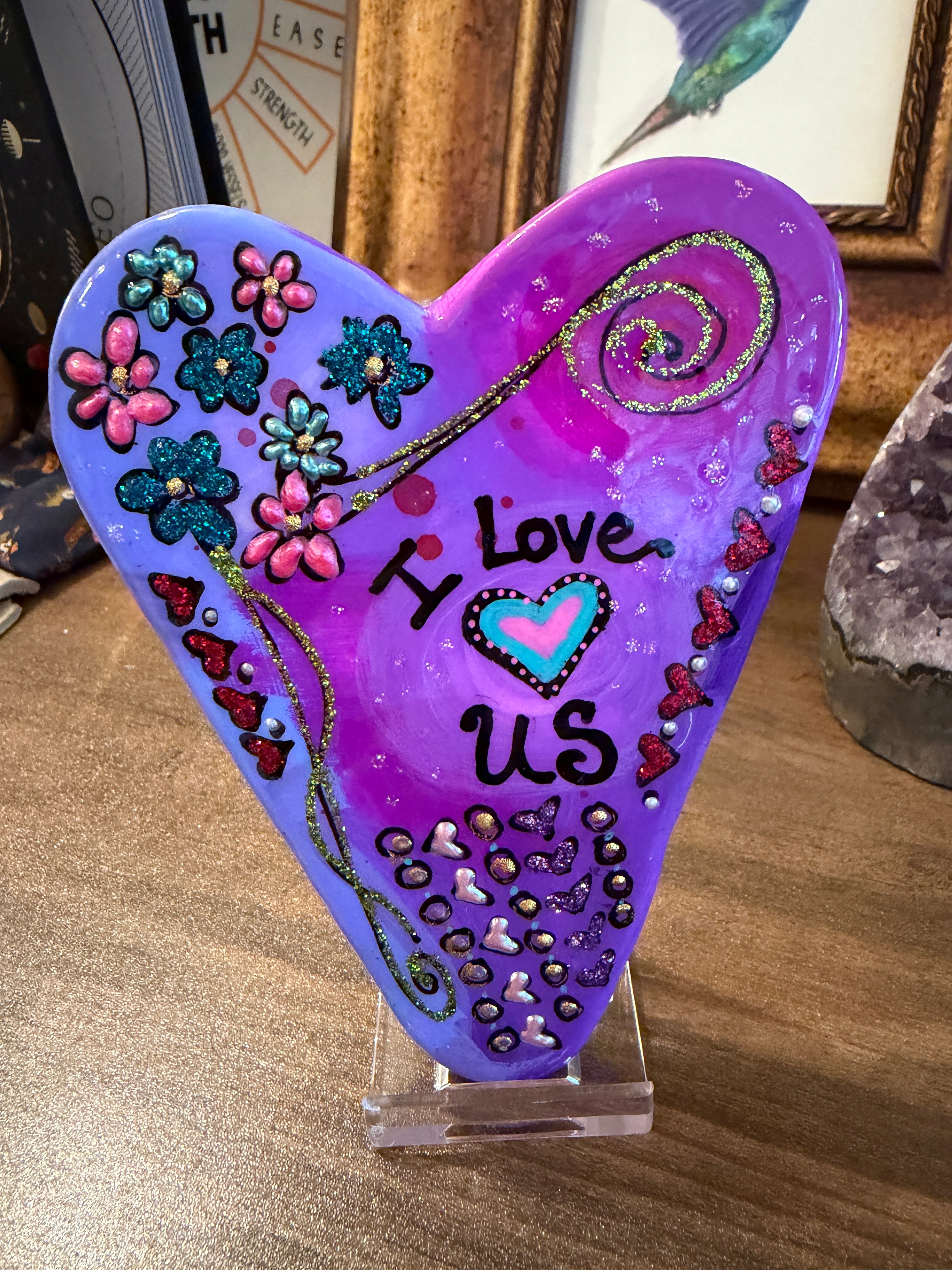 Decorative purple heart-shaped stone with floral designs and text on an acrylic stand.