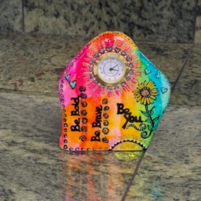 Colorful hand-painted clock with motivational phrases on a stone surface