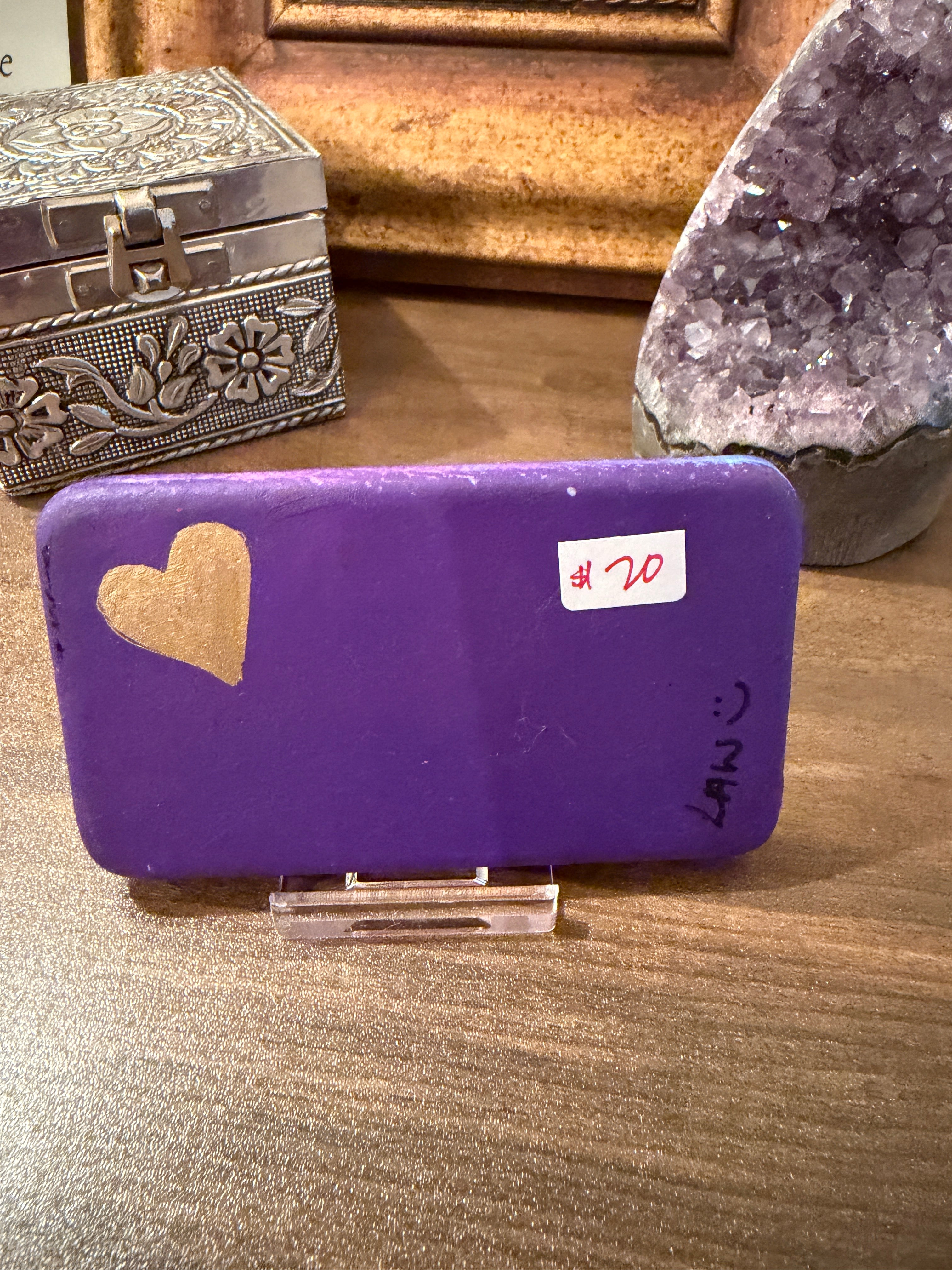 Purple painted pocket stone with a gold heart on a wooden surface