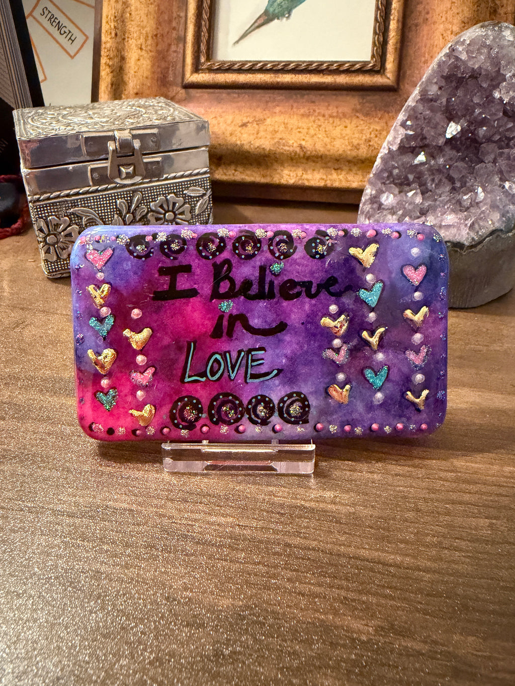 Decorative handpainted stone with 'I Believe in Love' text on a wooden surface