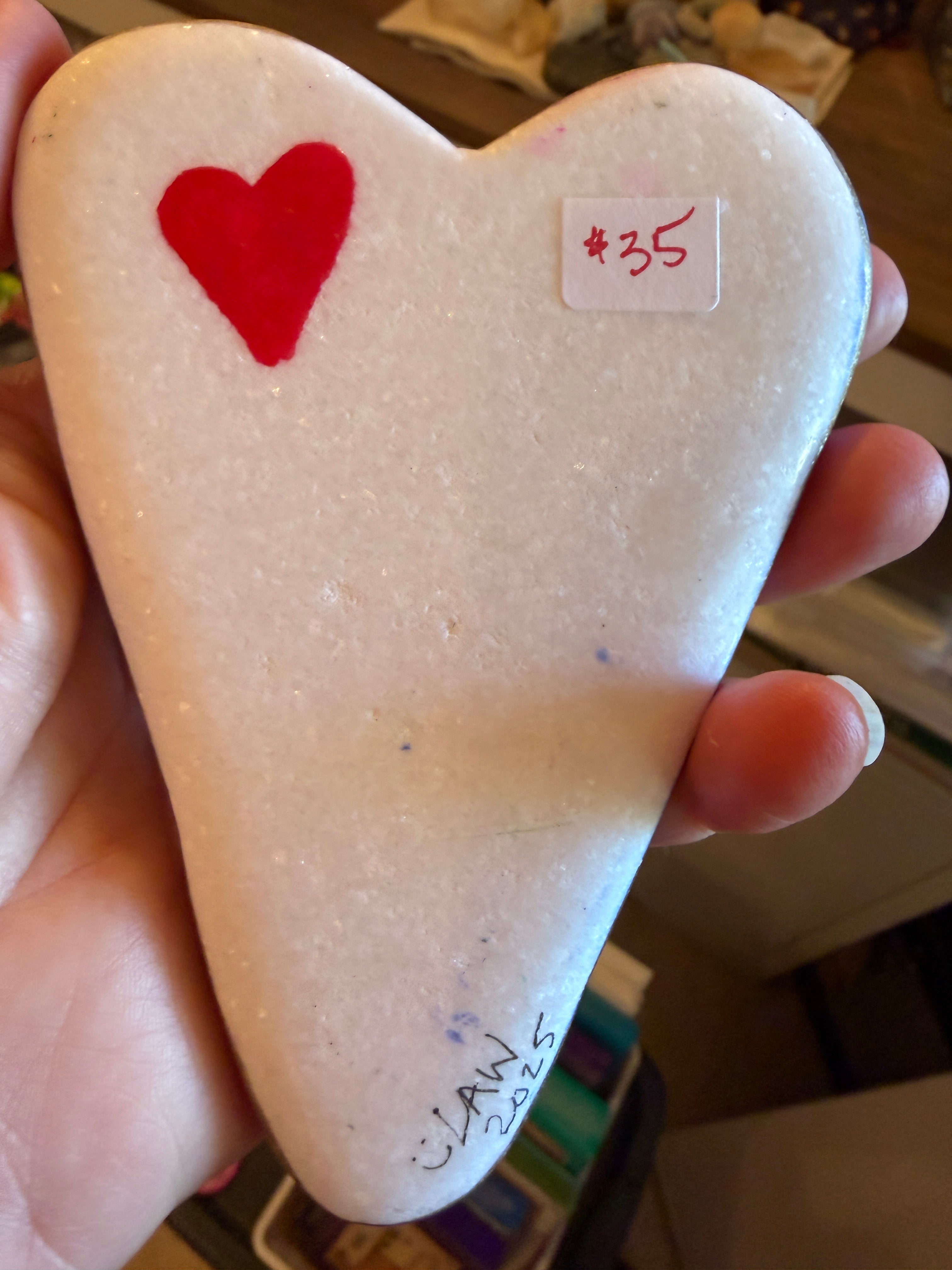 Heart-shaped stone with a red heart and text, held in a hand.
