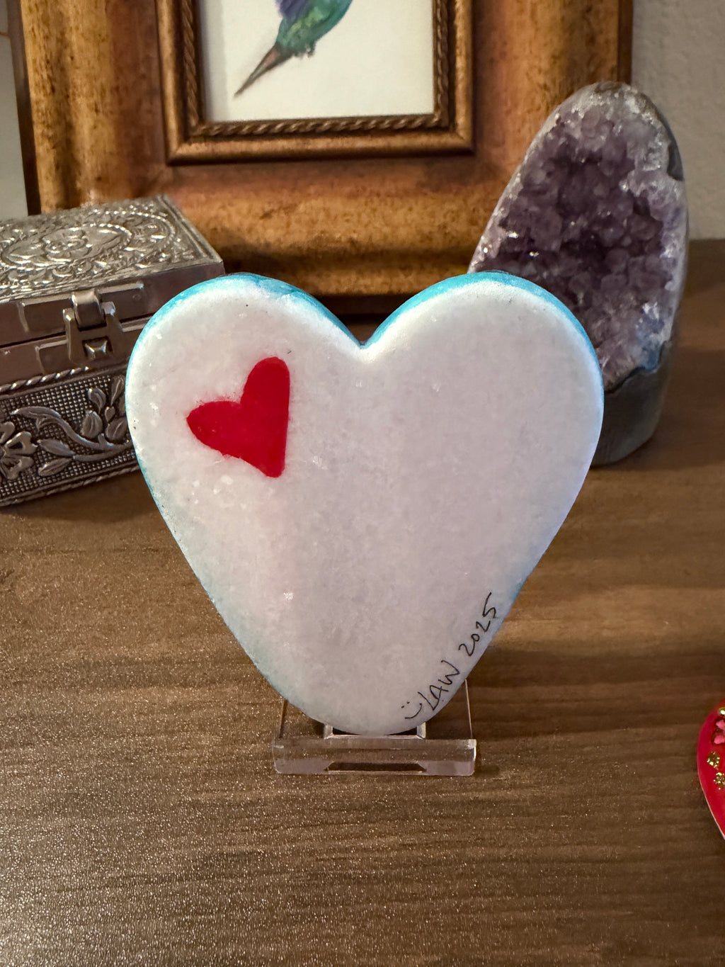 Heart-shaped painted stone with a red heart inside, placed on a textured surface.