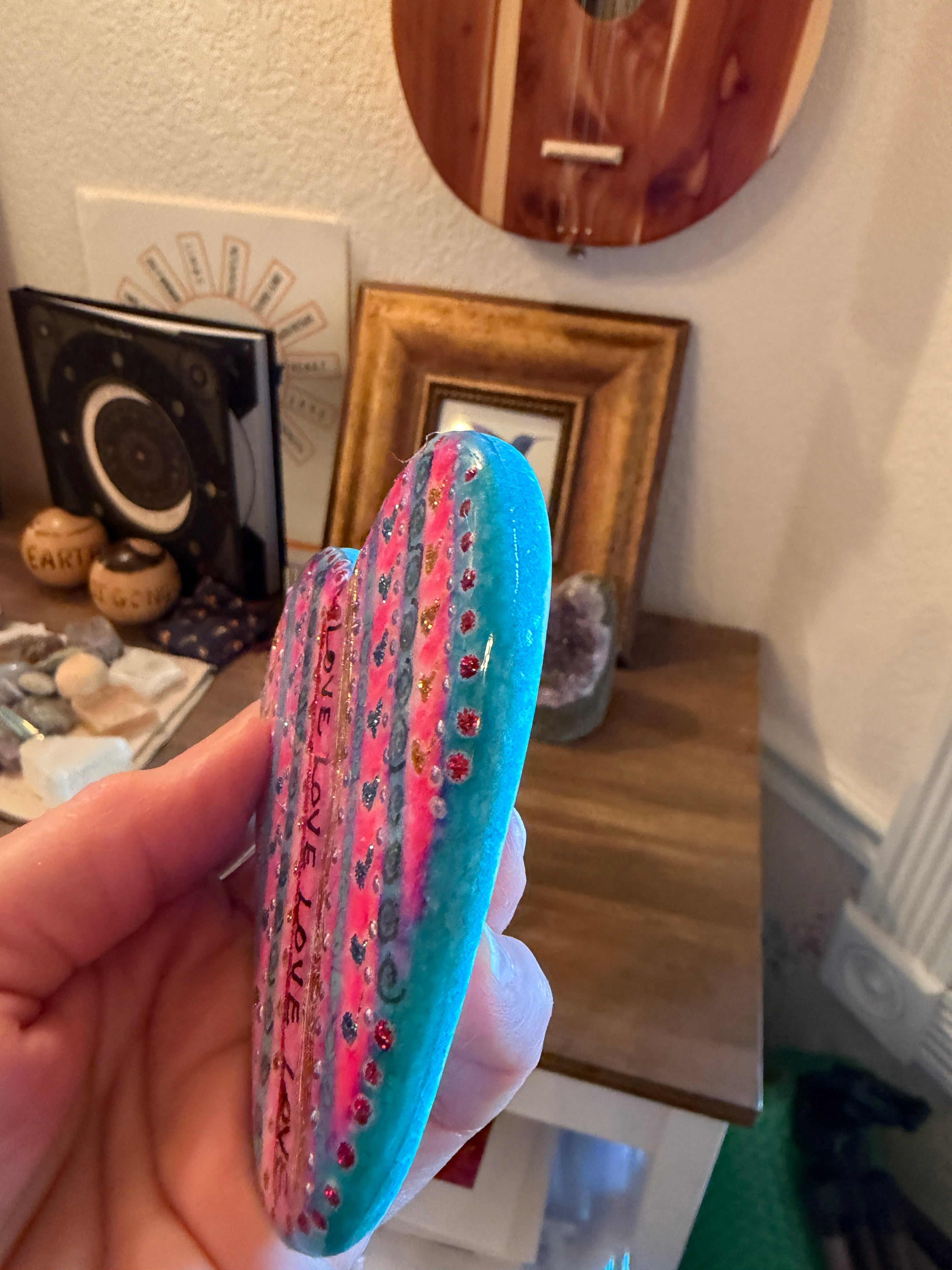 Hand holding a colorful painted heart with 'LOVE' text against a blurred indoor background