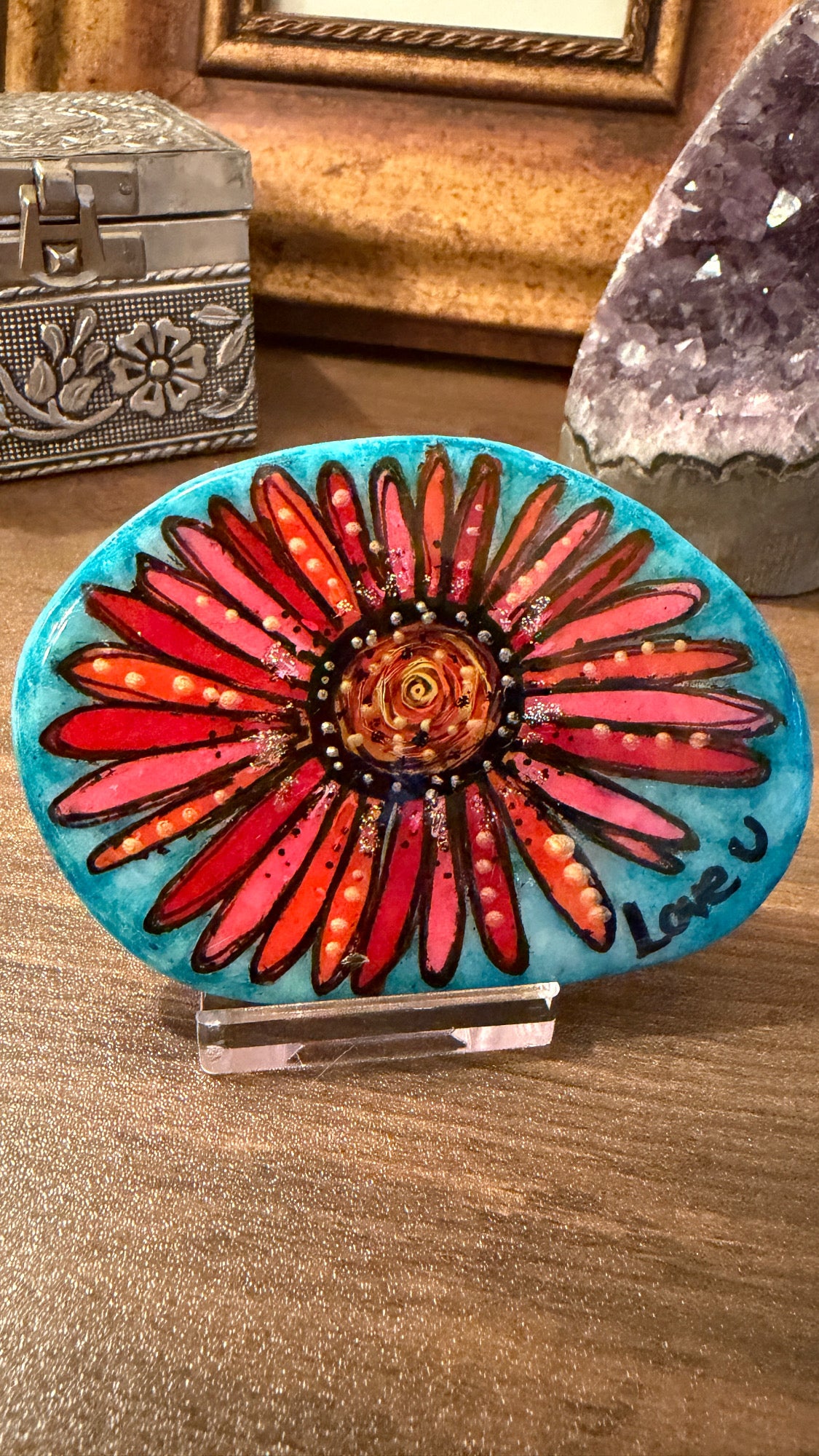 Decorative stone with a red floral design on a blue background, placed on a wooden surface.